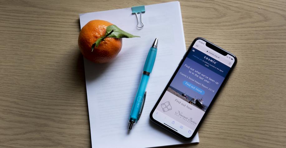 Notebook with a phone, pen and an orange sat on top.