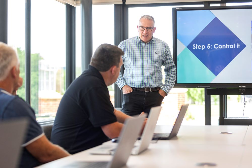 A senior consultant standing in front of a screen carrying out a presentation to a board room of leaders