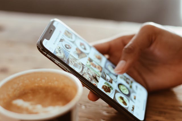 Person scrolling through a social media feed on a mobile phone with a coffee.
