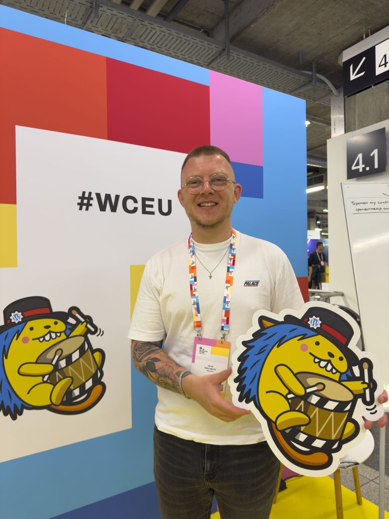 Man smiling whilst holding a cardboard cutout of the WordPress mascot "Wapuu"