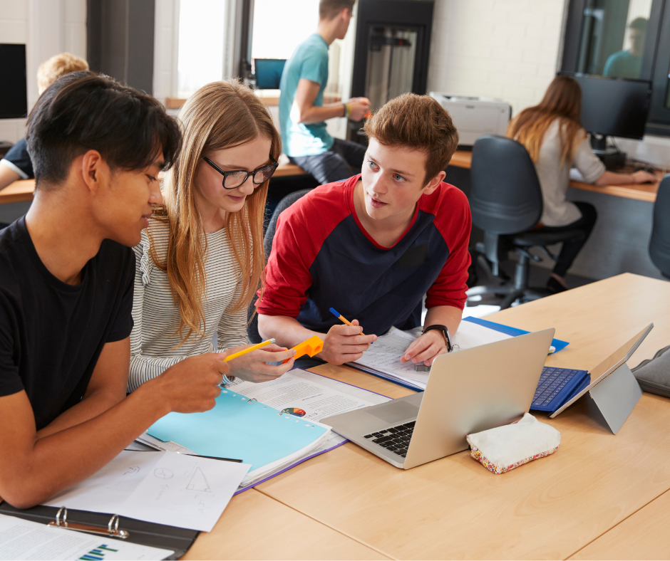 teenagers sat at desk in classroom in front of a laptop