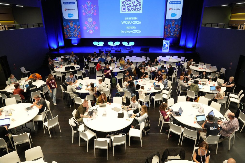 WordPress contributors working on laptops in a large room full of tables